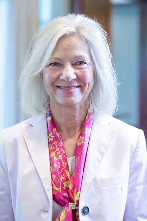Portrait of Pam Olsen in a pale pink jacket and bright pink patterned scarf